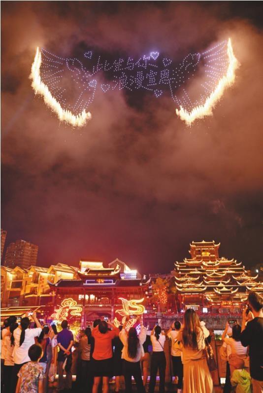 国庆中秋假期，人们走出家门，悦享假日时光。图为10月2日晚，游客在湖北省宣恩县城兴隆老街观看无人机烟花秀。新华社发