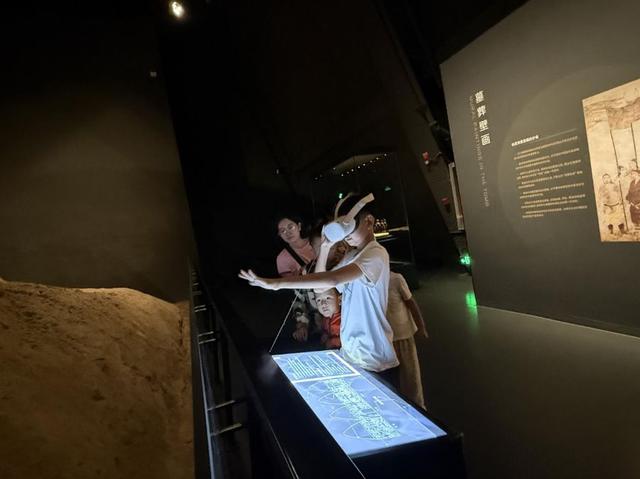 游客站在夯土堆旁，戴上VR眼镜，“走入”《宴饮图》壁画。新华网 王梦佳 摄